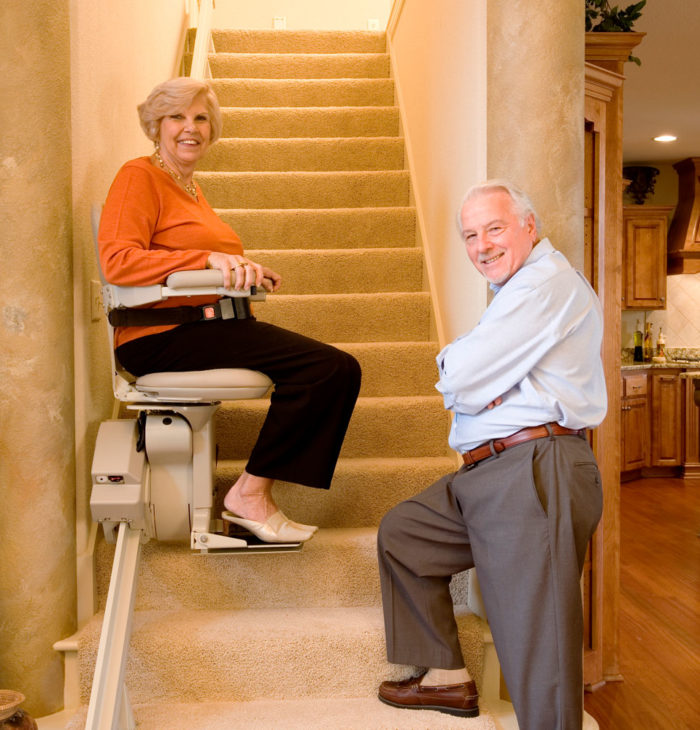 Old woman on stairlift with man observing